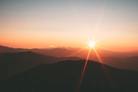 The sun is rising over a gentle mountain range. The sky is colored pink and orange.